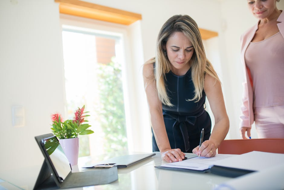 Woman signing documents at a desk with a colleague nearby